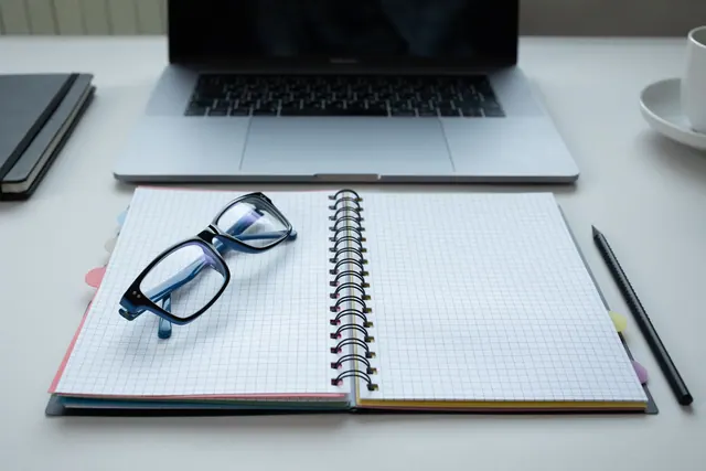 A clean and organized desk with a laptop, notepad, eyeglasses, and pencil, ideal for productivity.