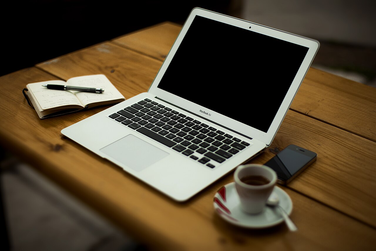 Arbeitsplatz mit Notebook, Notizbuch, Smartphone und Kaffeetasse auf Holztisch