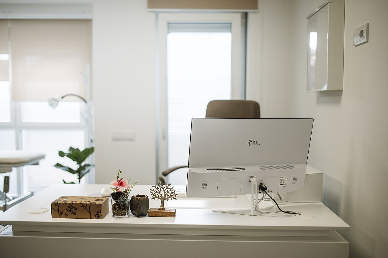Weißer Schreibtisch mit Monitor und dekorativen Objekten vor hellem Bürohintergrund