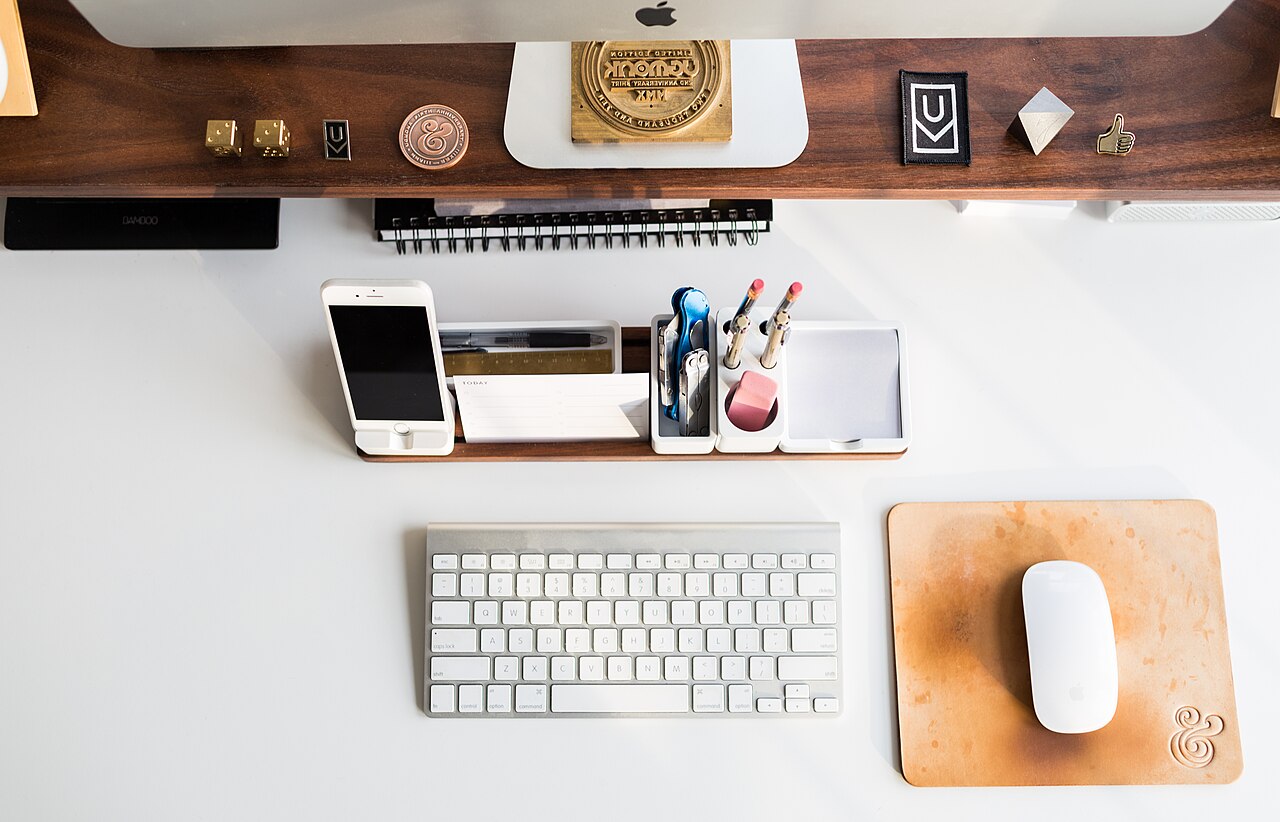 Aufgeräumter Schreibtisch von oben mit Computer, Tastatur, Smartphone und Büromaterial