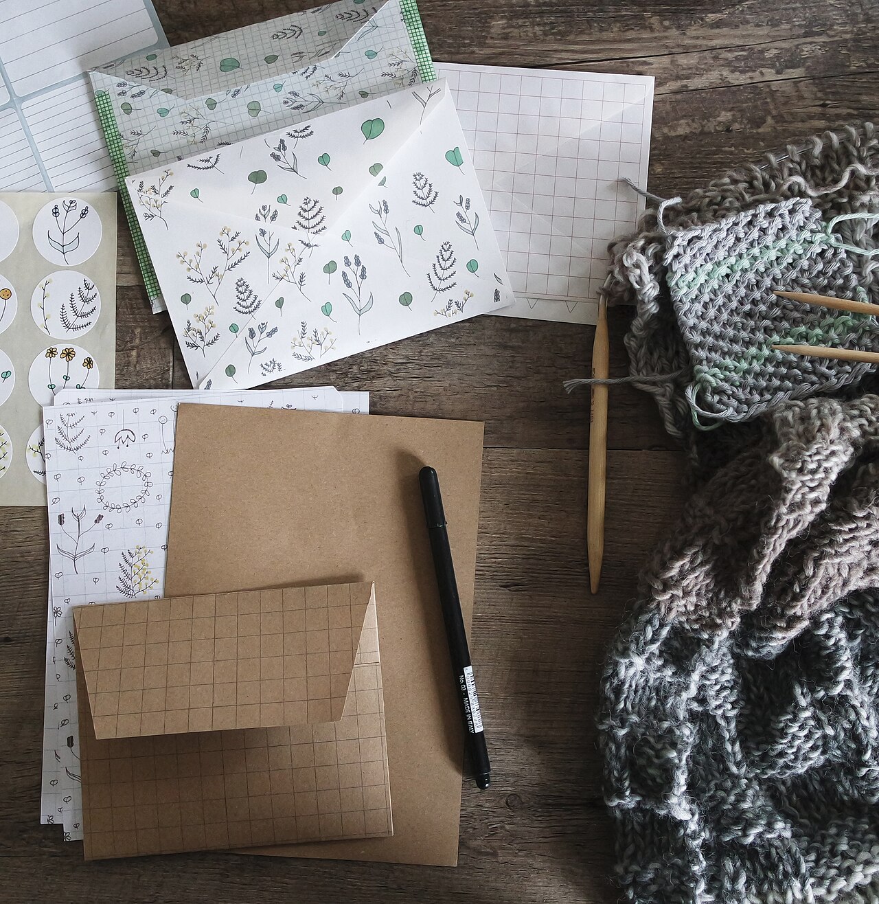 Papierbögen, Umschläge und Strickzeug auf Holztisch