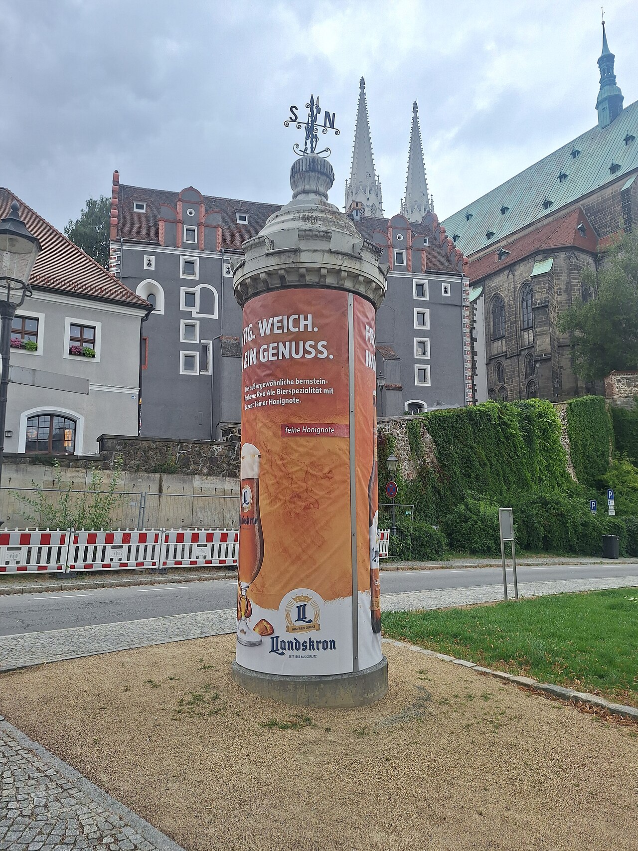 Runde Litfaßsäule mit Werbung für Landskron Bier an einer Straße