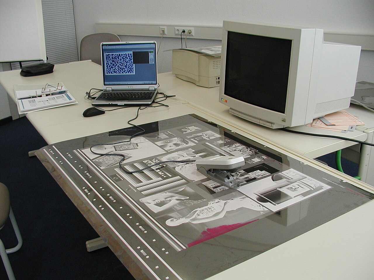 Arbeitsplatz mit Laptop, Röhrenmonitor und Druckmaterialien