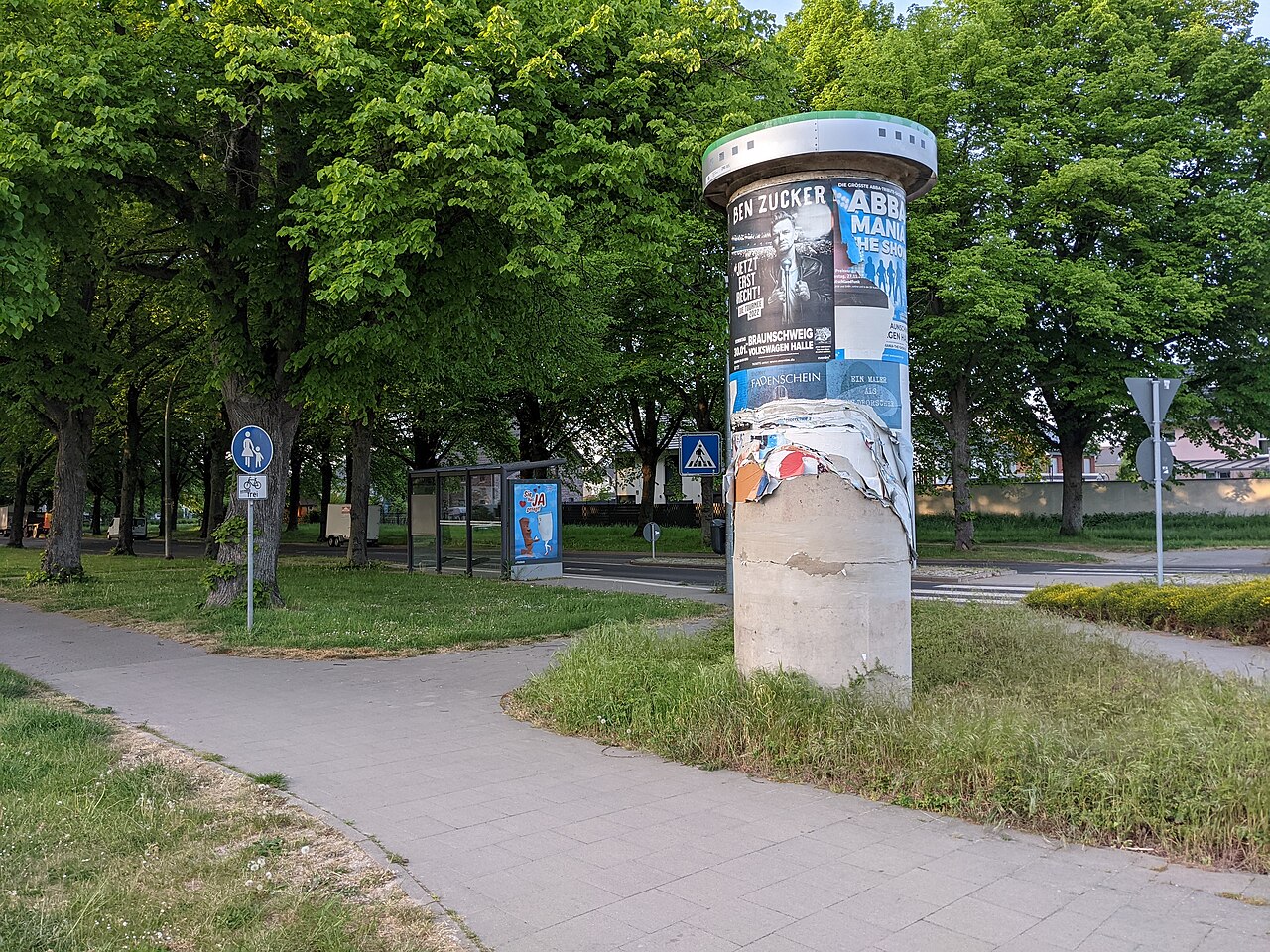 Litfaßsäule mit zerrissenen Plakaten an einem Fußweg