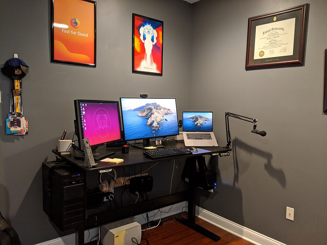 Homeoffice-Arbeitsplatz mit drei Monitoren, Mikrofon und Kopfhörern vor grauer Wand